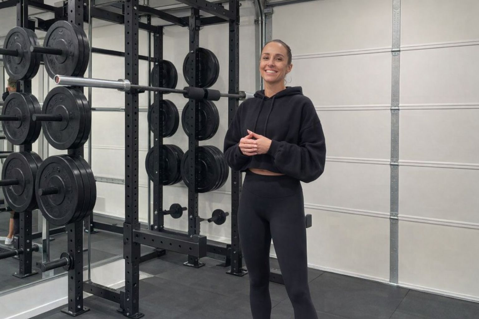 Kvinna i träningskläder framför ett robust power rack i ett hemmagym.