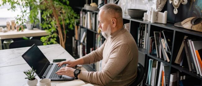 Skäggig man skriver vid laptop i ett ljust hemmakontor